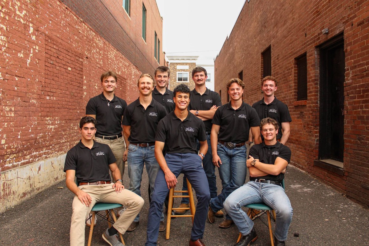 The nine men of Iron Circle in matching black Iron Circle polos, gathered in a brick alley.