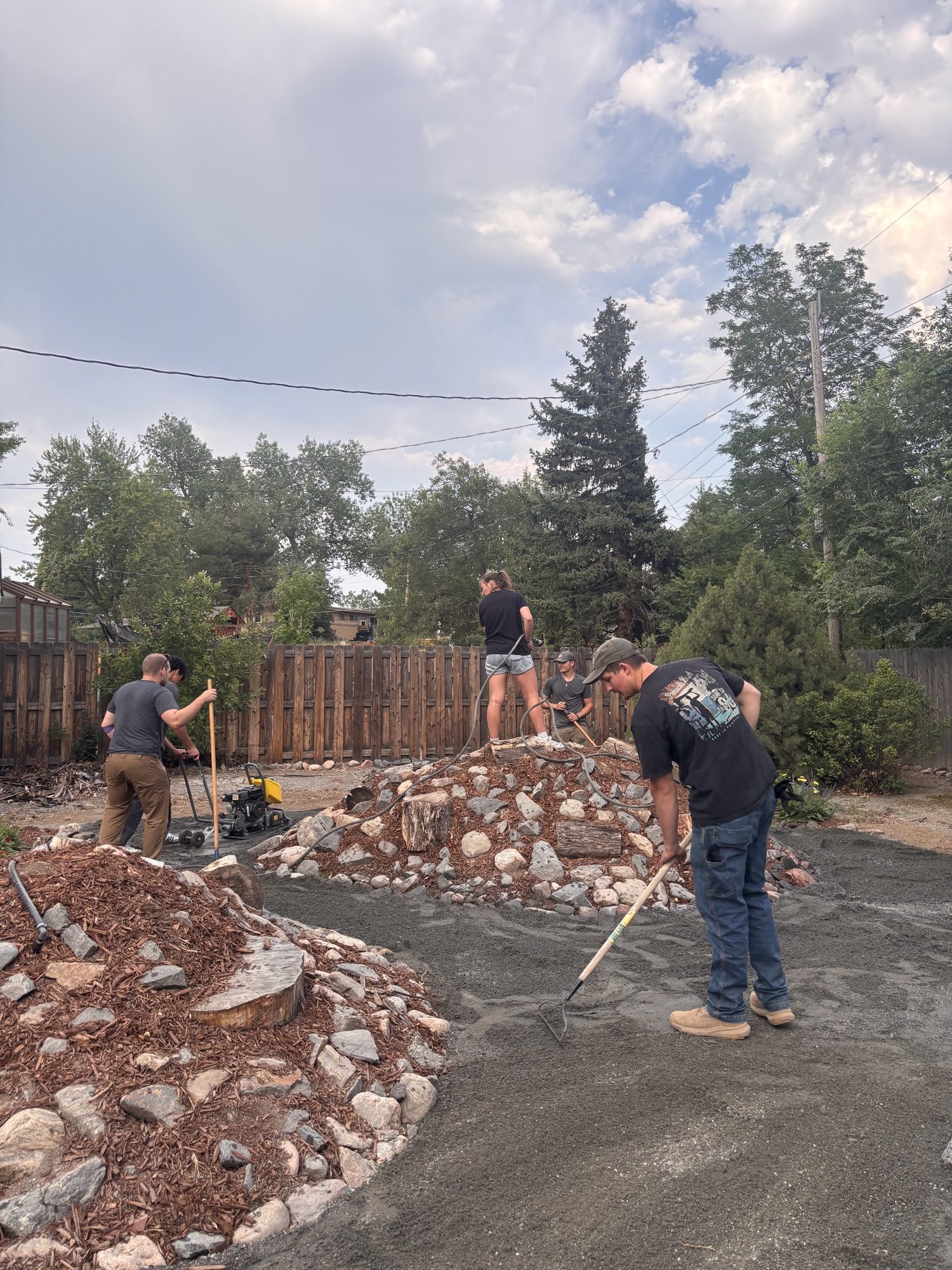 Spreading and raking base gravel across the yard, with the compactor running behind.